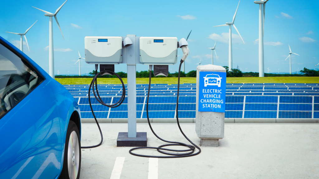 car charging next to solar panels and wind turbines